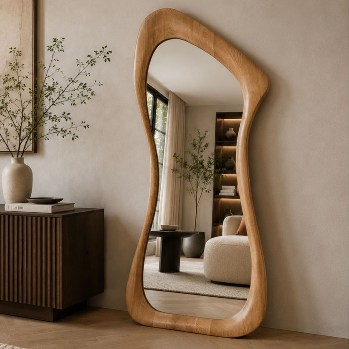 An organic-shaped wooden floor mirror with a natural light oak frame, leaning against a beige wall in a modern, minimalist living room setting.