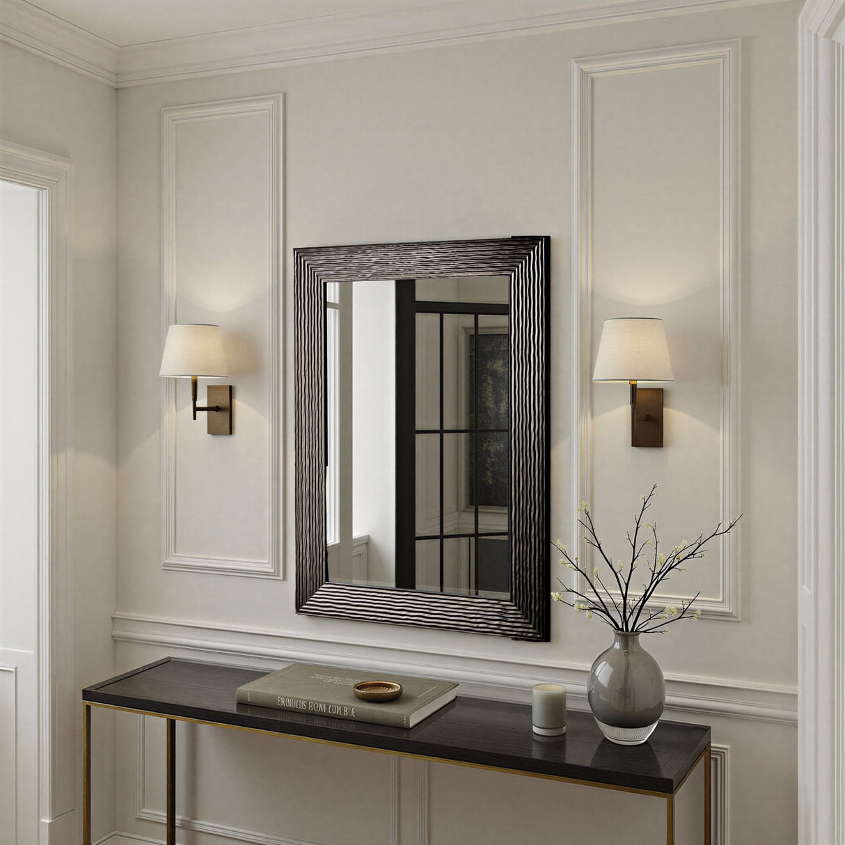 Decorative mirror with black frame on a wall above a console table with a vase and books.