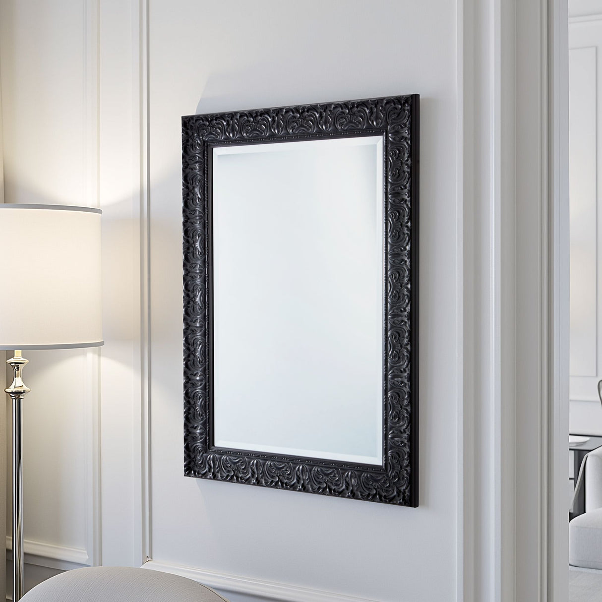 Decorative black-framed mirror on a white wall with a lamp to the left.