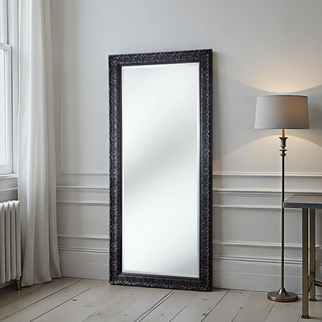 Decorative floor mirror with ornate black frame in a room with a lamp and radiator.