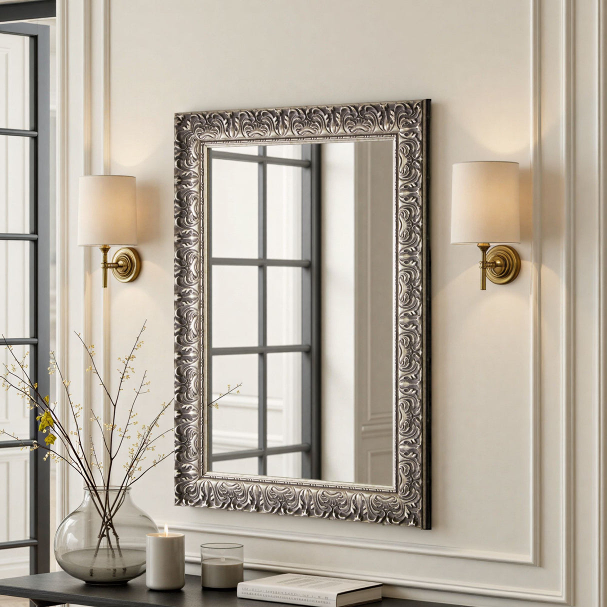 Decorative wall mirror with ornate frame in a room with wall sconces and a vase.