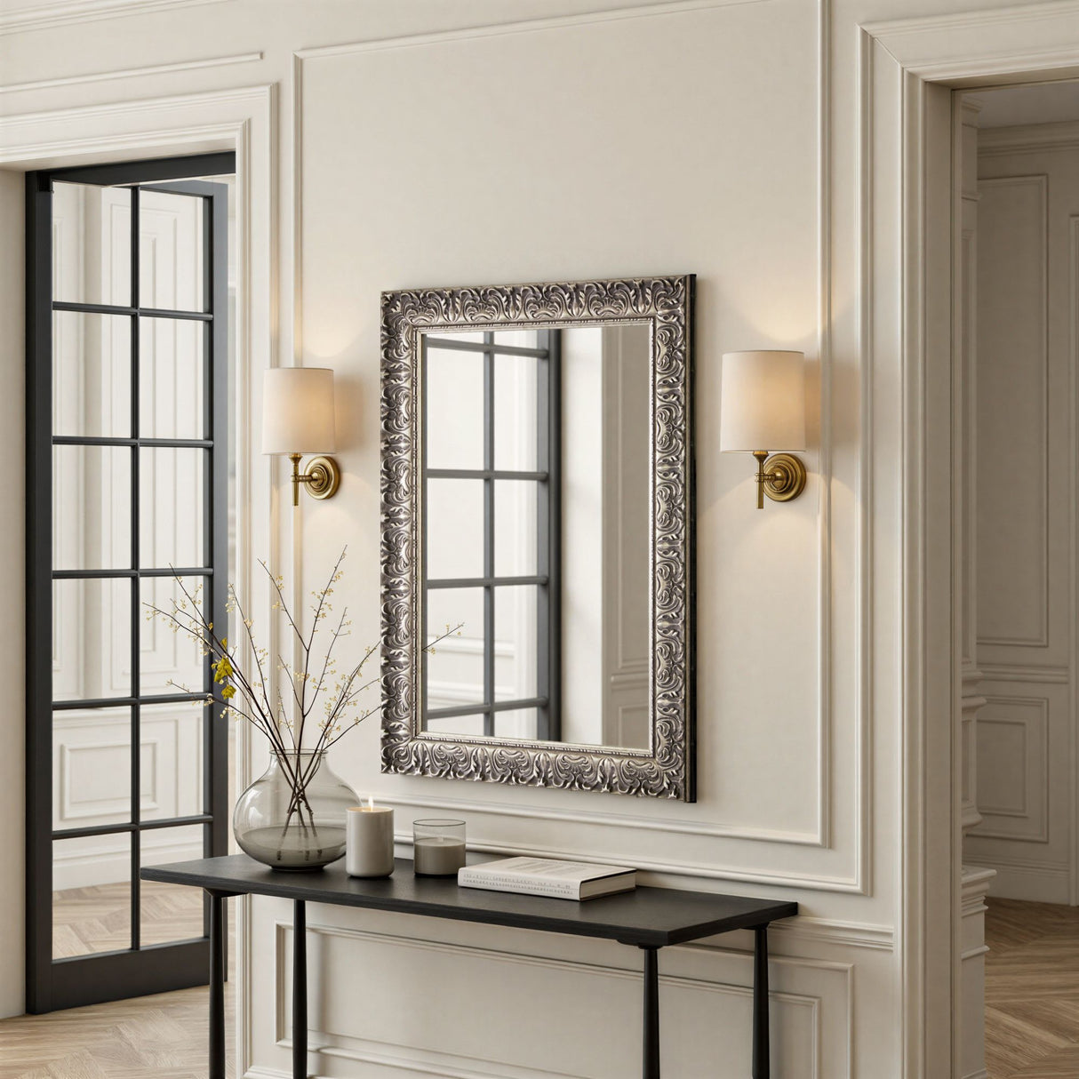 Decorative mirror with ornate frame on a wall with sconces and a console table.