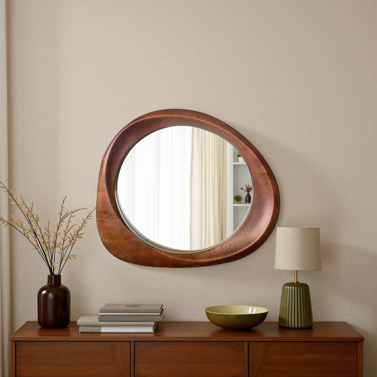 Round wooden mirror on a wall with a lamp and books on a wooden console table.