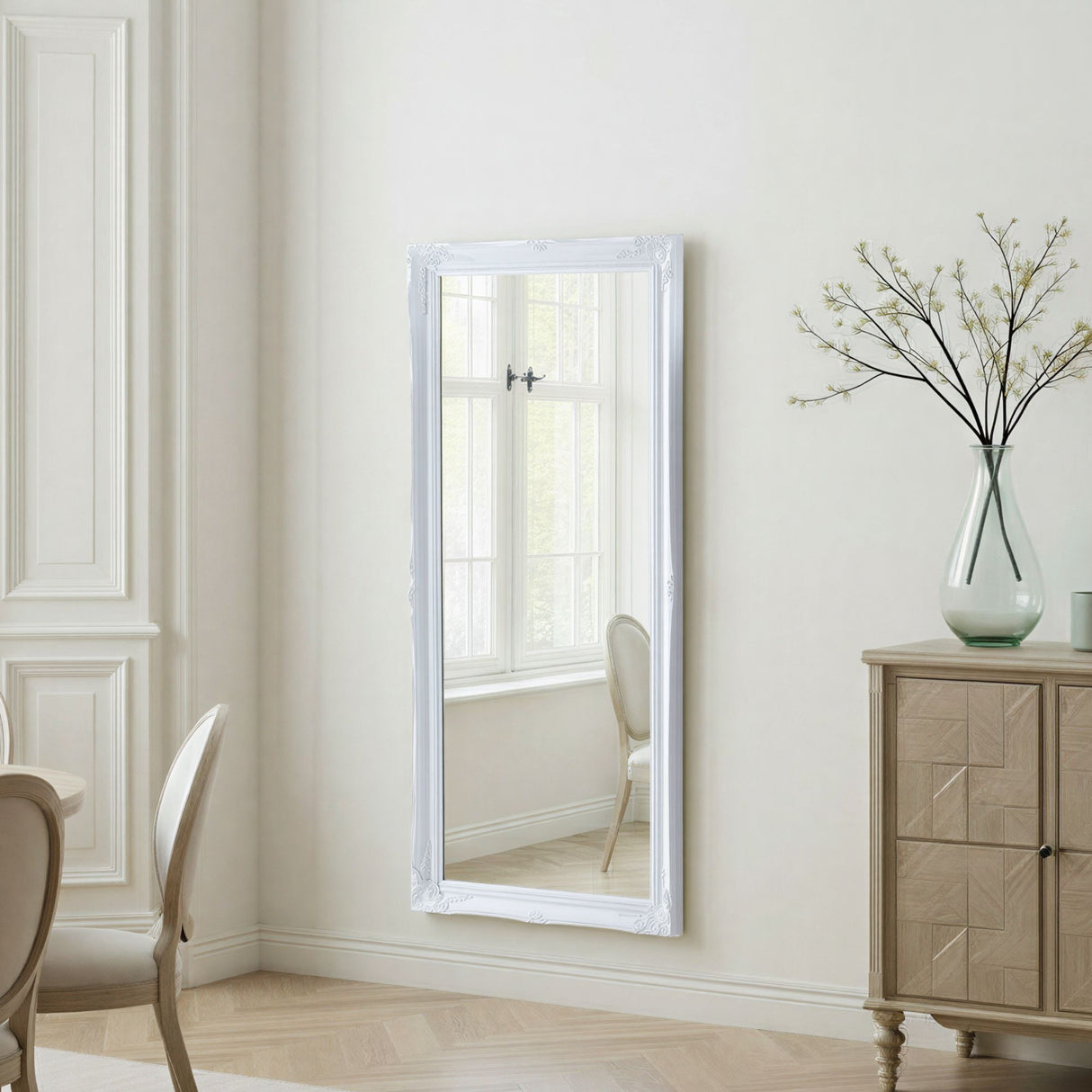 Full-length mirror with white frame leaning against a wall in a room with a wooden cabinet and chair.
