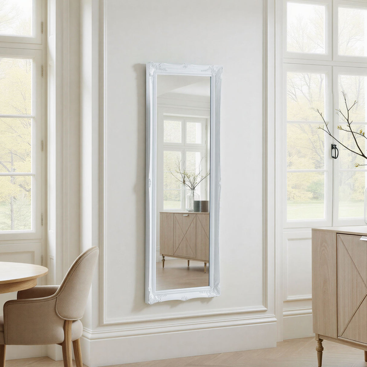 Full-length mirror with white frame on a wall in a bright room with large windows.