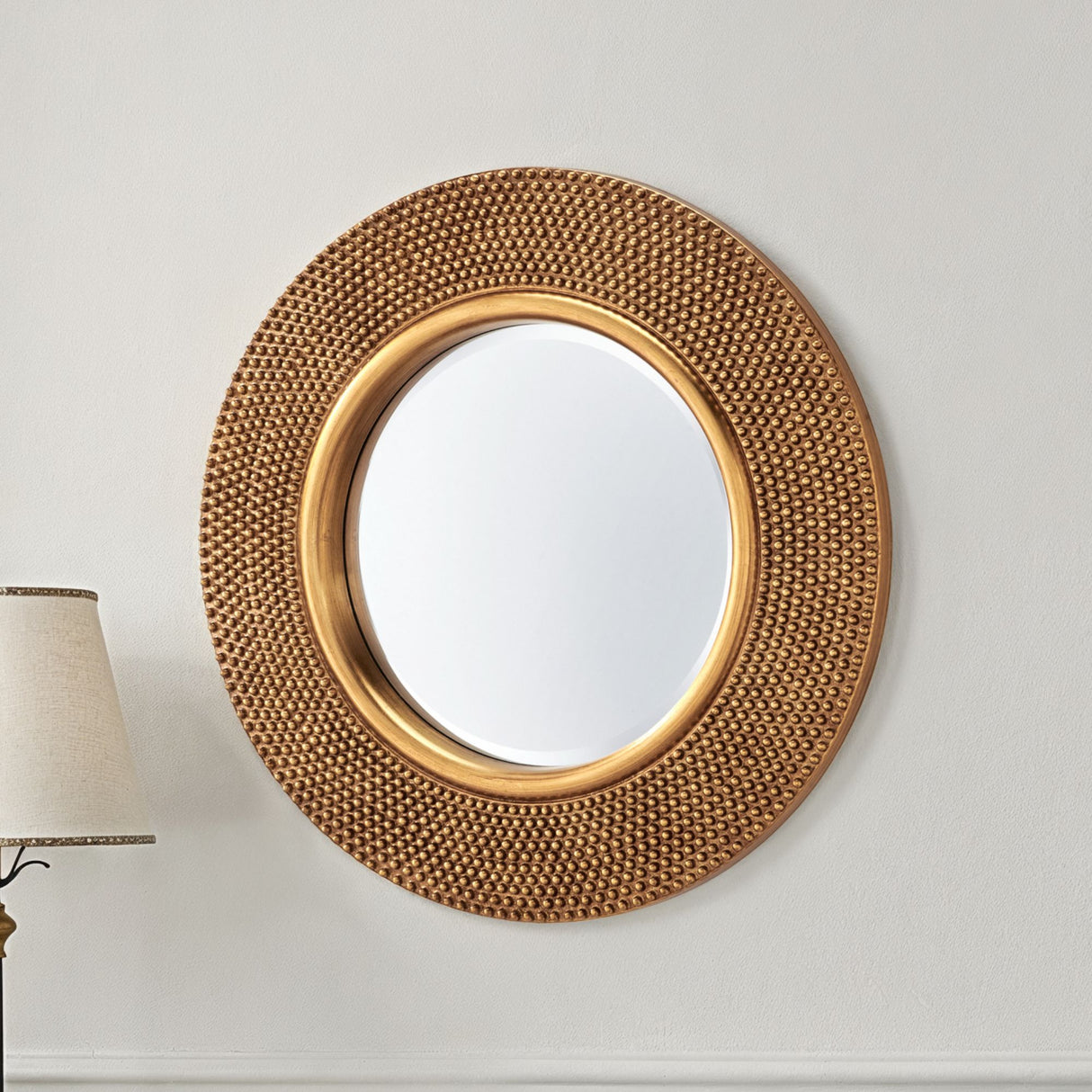 Decorative gold mirror on a white wall with a lamp in the corner.