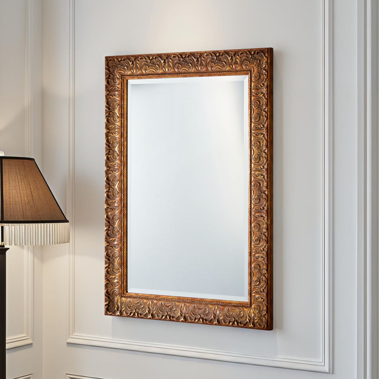 Decorative gold-framed mirror on a white wall with a lamp in the corner.