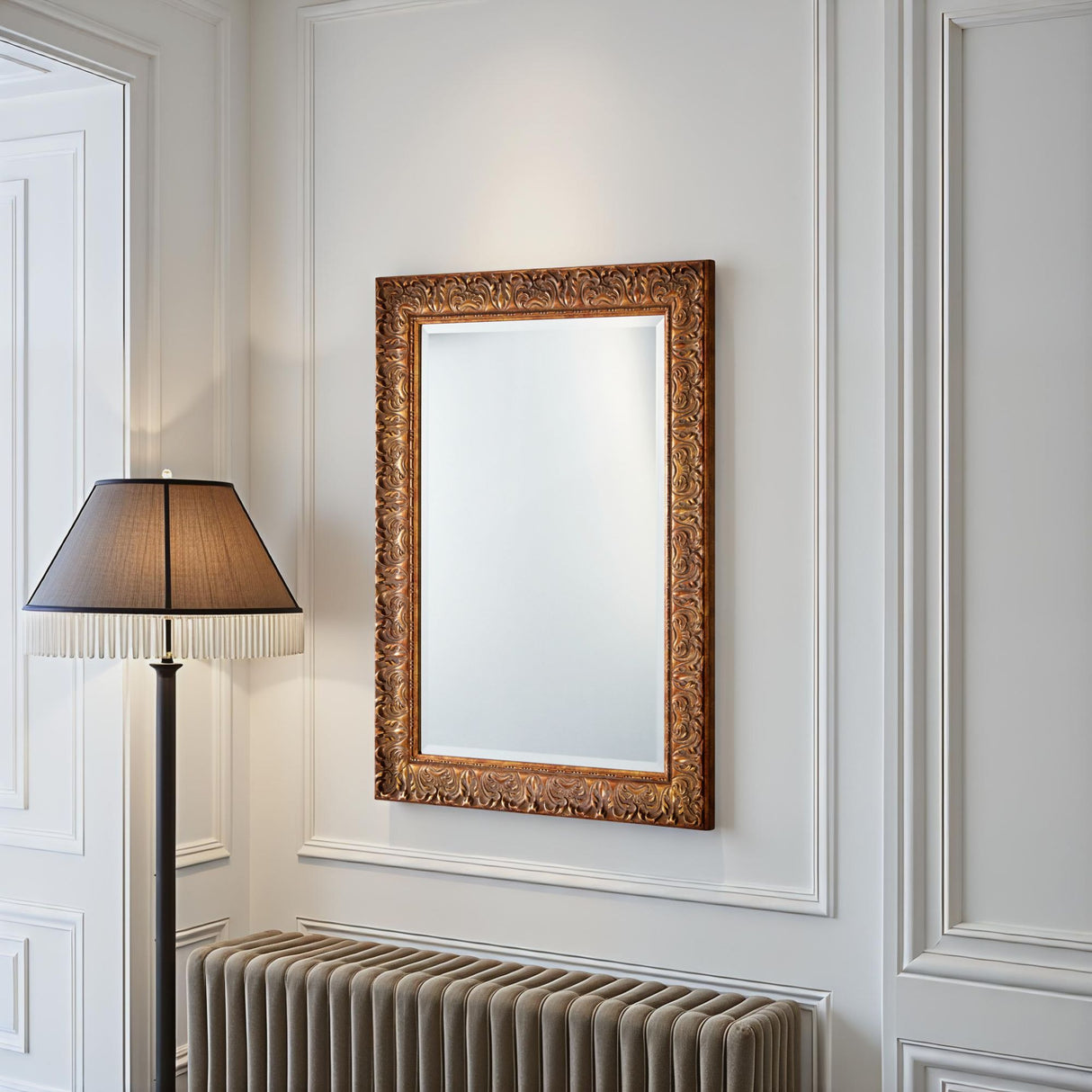 Decorative mirror with gold frame on a wall with white paneling and a floor lamp.