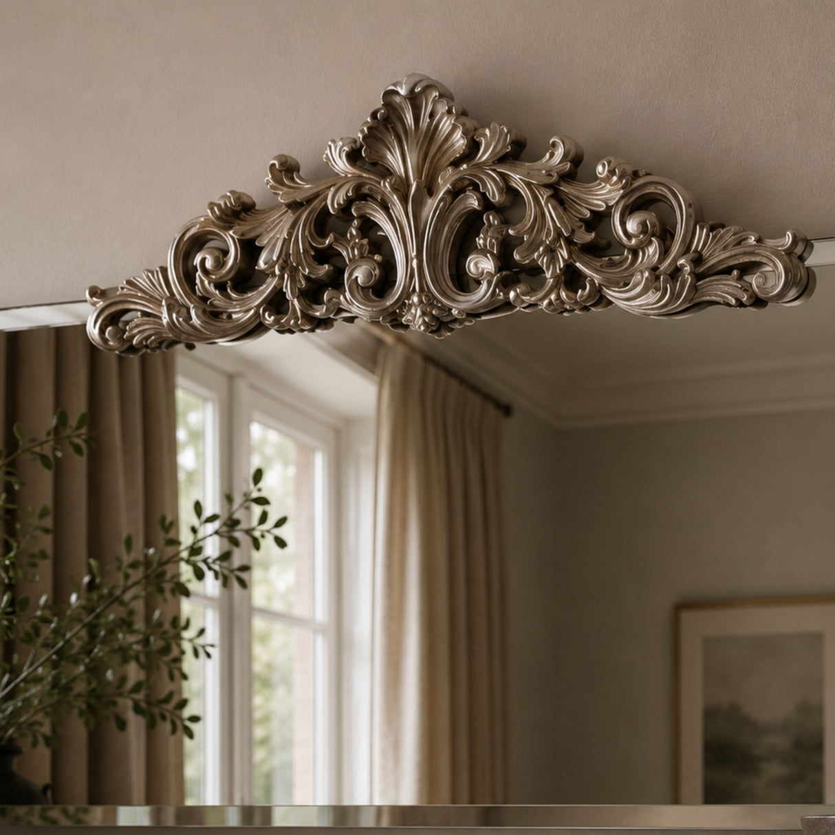 An ornate silver mirror frame with a highly detailed baroque-style acanthus leaf and scrollwork top, shown reflecting a neutral-toned room with beige curtains and a window.
