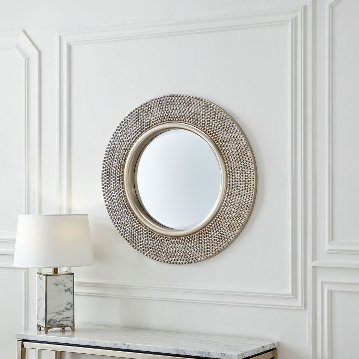 Decorative round mirror with intricate design on a white wall with molding