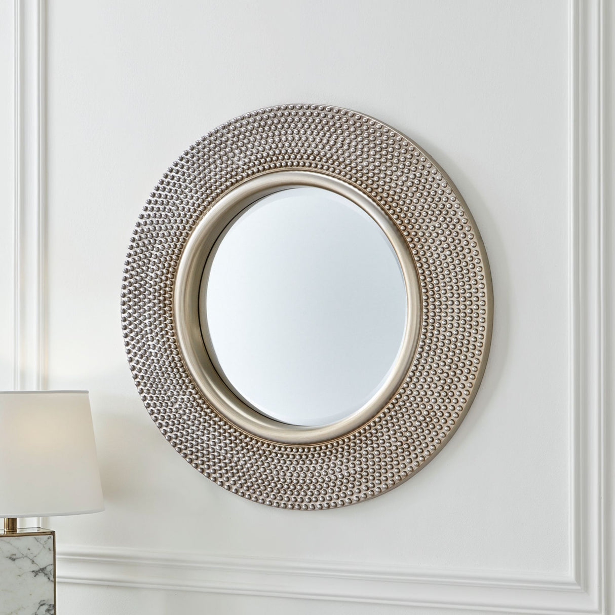 Round decorative mirror with a textured frame on a white wall.