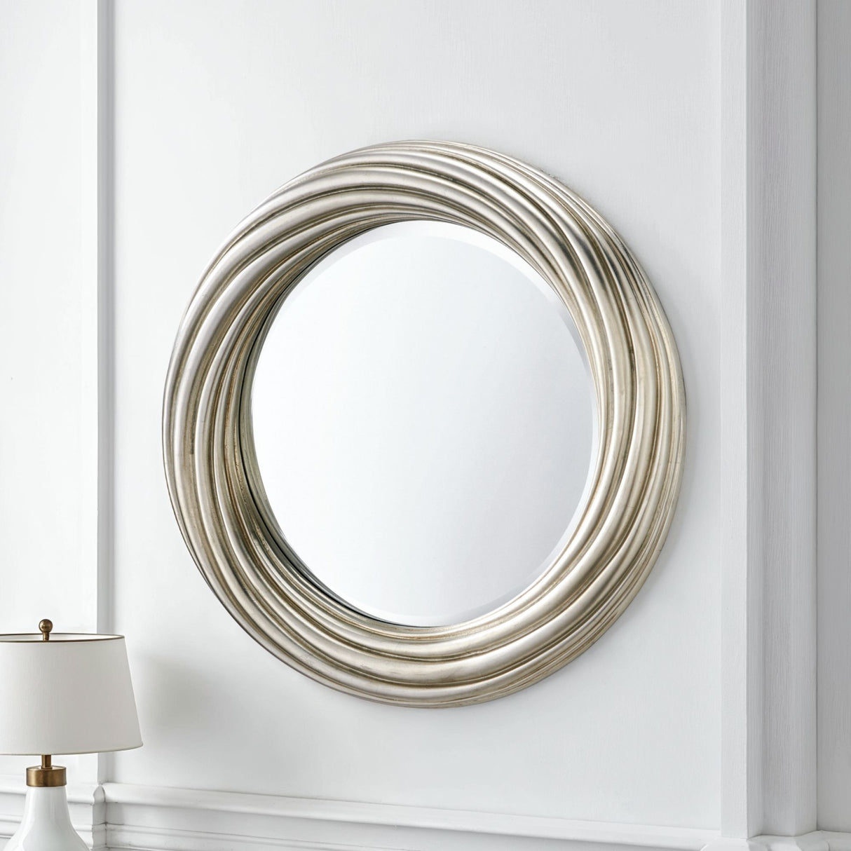 Decorative round mirror with a silver frame on a white wall.