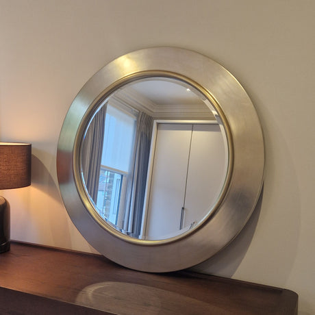 Round metallic mirror on a wall with a lamp to the left