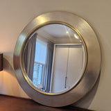 Round metallic mirror on a wall with a reflection of a room.