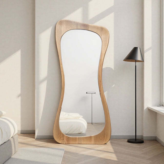 Wooden floor mirror in a room with a lamp and bed.
