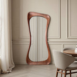 Wooden floor mirror with wavy design in a room with beige walls and a dining table.