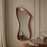 Wooden wall mirror with wavy design on a beige paneled wall.