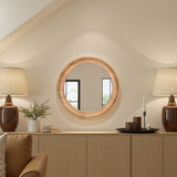 Round wooden mirror on a wall above a wooden console table with decor items.