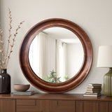 Round wooden mirror on a wooden dresser with decorative items.