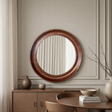 Round wooden mirror on a wall with a sideboard and decor items in a room.