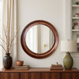 Round wooden mirror on a wall above a wooden console table with decorative items.