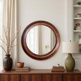 Round wooden mirror on a wall above a wooden console table with decorative items.