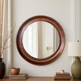 Round wooden mirror on a wall with decorative items below