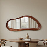 Wooden mirror with wavy design on a beige wall above a wooden table with decor items.
