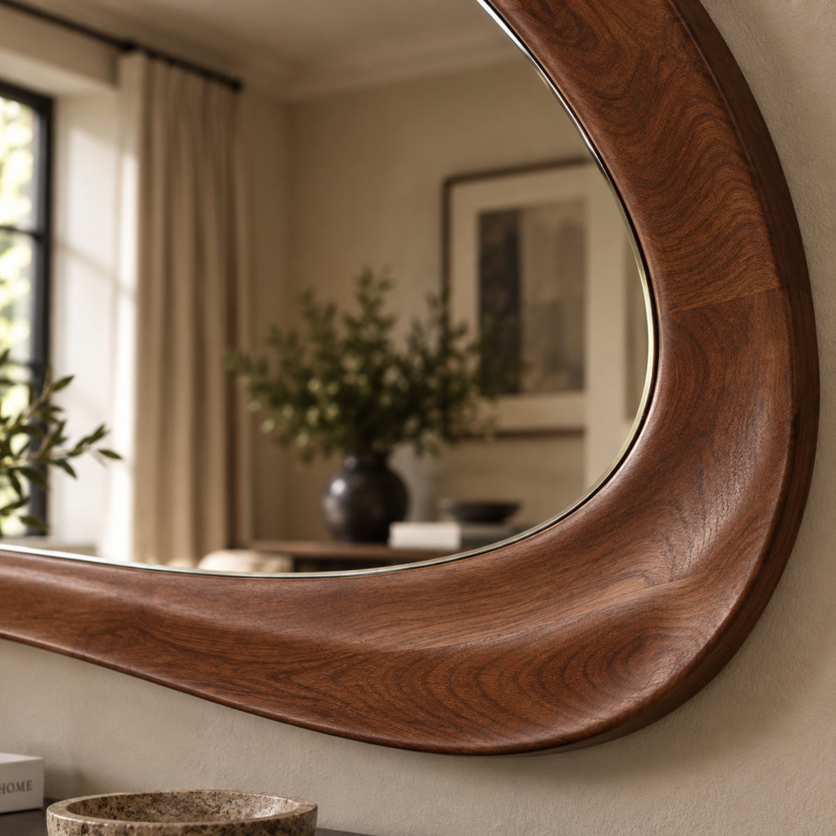 A close-up of a large, uniquely shaped wall mirror with a thick, curved dark brown wooden frame, mounted on a beige wall in a softly lit room.