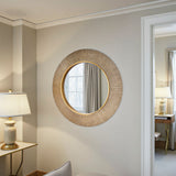 Round woven mirror on a wall with a lamp and curtain in the background