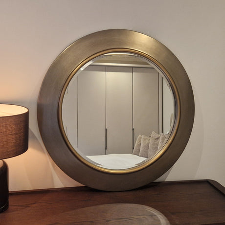 Round mirror with a gold frame on a wooden surface, reflecting a room interior.