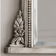 Close-up of an ornate silver mirror frame corner with a floral relief and beaded vertical detail, set against a light gray wall.