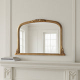 Decorative gold-framed mirror on a white wall above a fireplace.