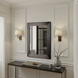 Decorative mirror with black frame on a wall above a console table with a vase and books.