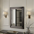 Decorative mirror with wavy frame on a wall with two lamps and a vase.