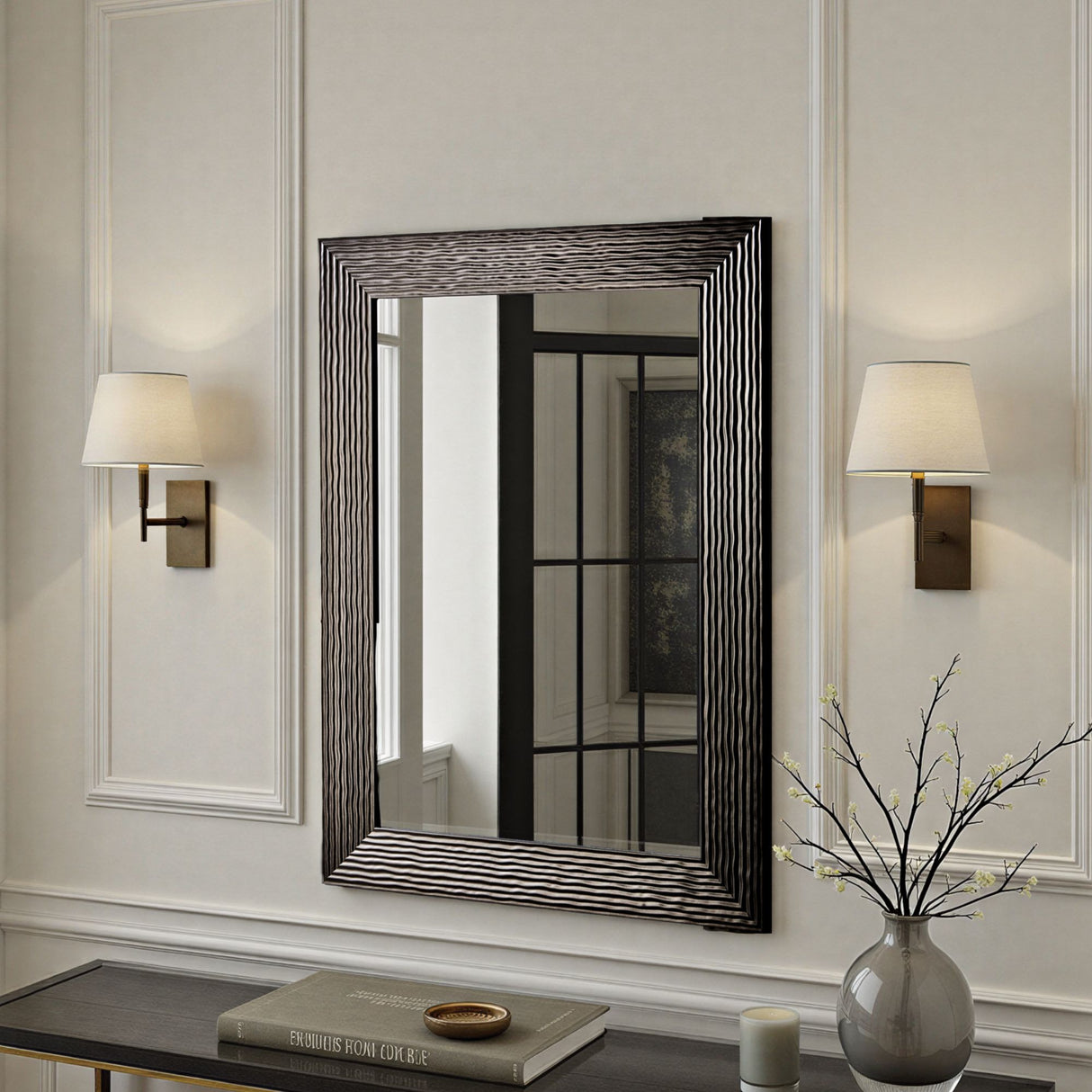 Decorative mirror with wavy frame on a wall with two lamps and a vase.