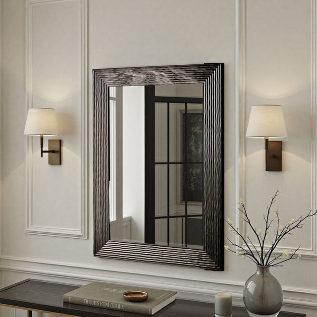Decorative mirror with wavy frame on a wall with two lamps and a vase.