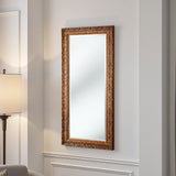 Decorative wall mirror with ornate gold frame on a light gray wall.