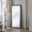 Decorative floor mirror with ornate frame in a room with a lamp and table.