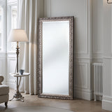 Decorative floor mirror with ornate frame in a room with a lamp and table.