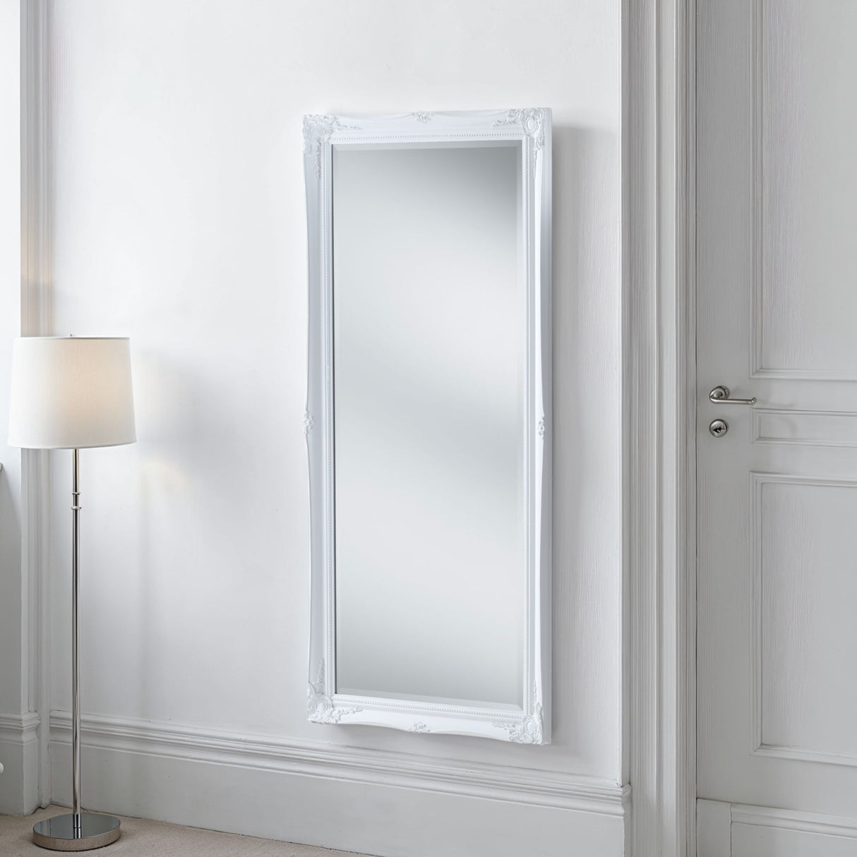 White framed mirror on a white wall with a floor lamp to the left.