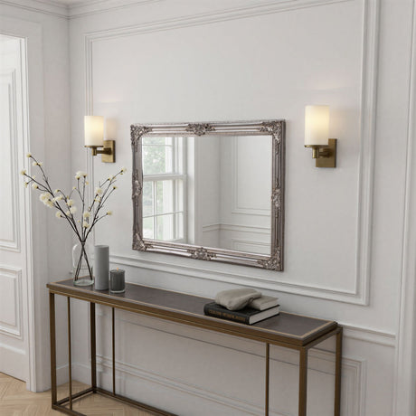 Decorative mirror on a wall above a console table with a vase and books.