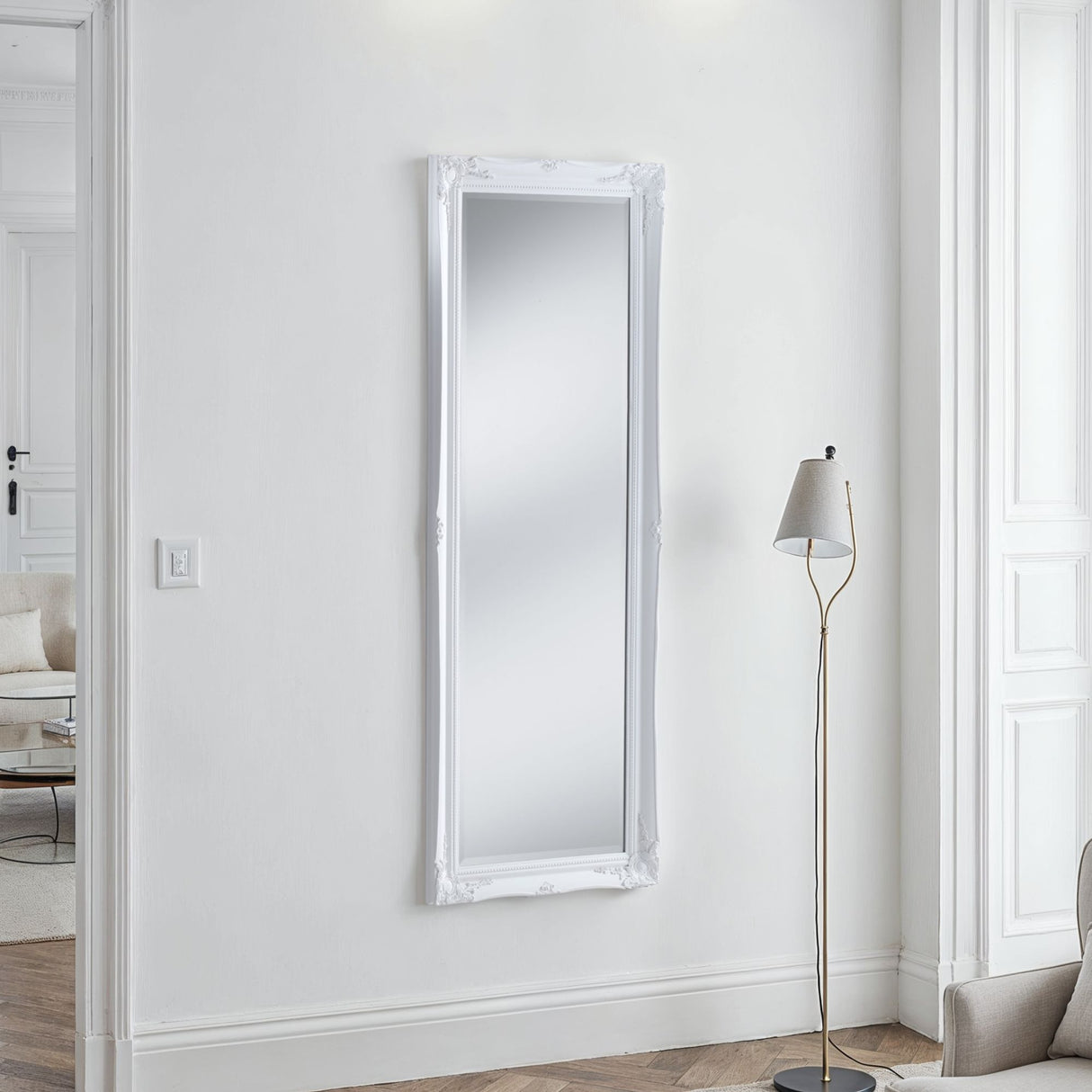 White-framed mirror on a white wall with a floor lamp in a minimalistic room.