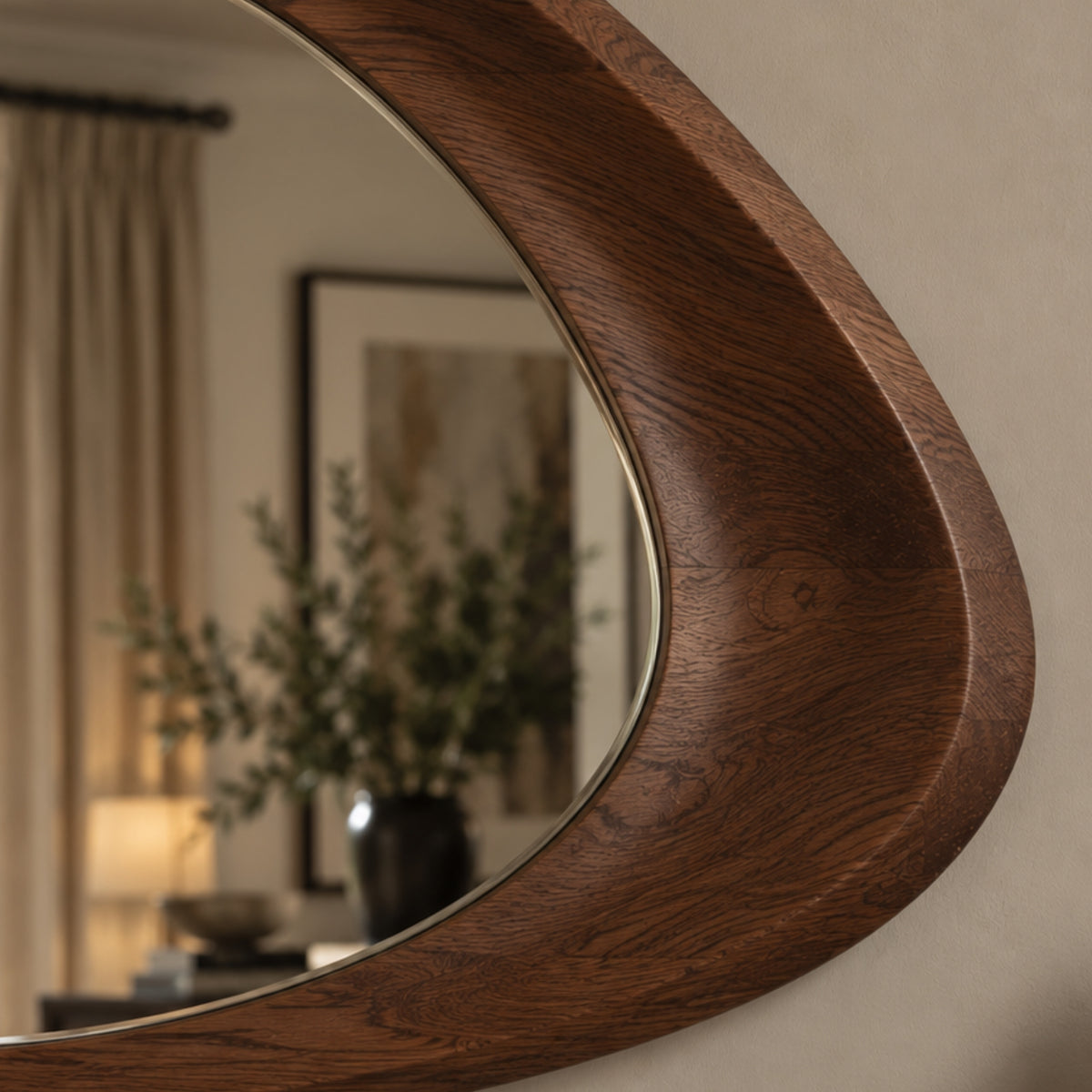 A close-up of a modern, curved wooden wall mirror with a rich dark brown wood grain finish and a thin brass inner trim, shown mounted on a beige wall with its reflection visible.