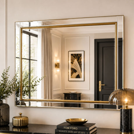 A large rectangular wall mirror with a thin gold frame hangs on a cream wall above a console table. The mirror reflects a classic interior with curtains, a door, and wall sconces.
