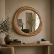 Round wooden wall mirror with a thick natural oak frame, mounted on a beige wall above a wooden console table styled with books, a vase, and dried branches.