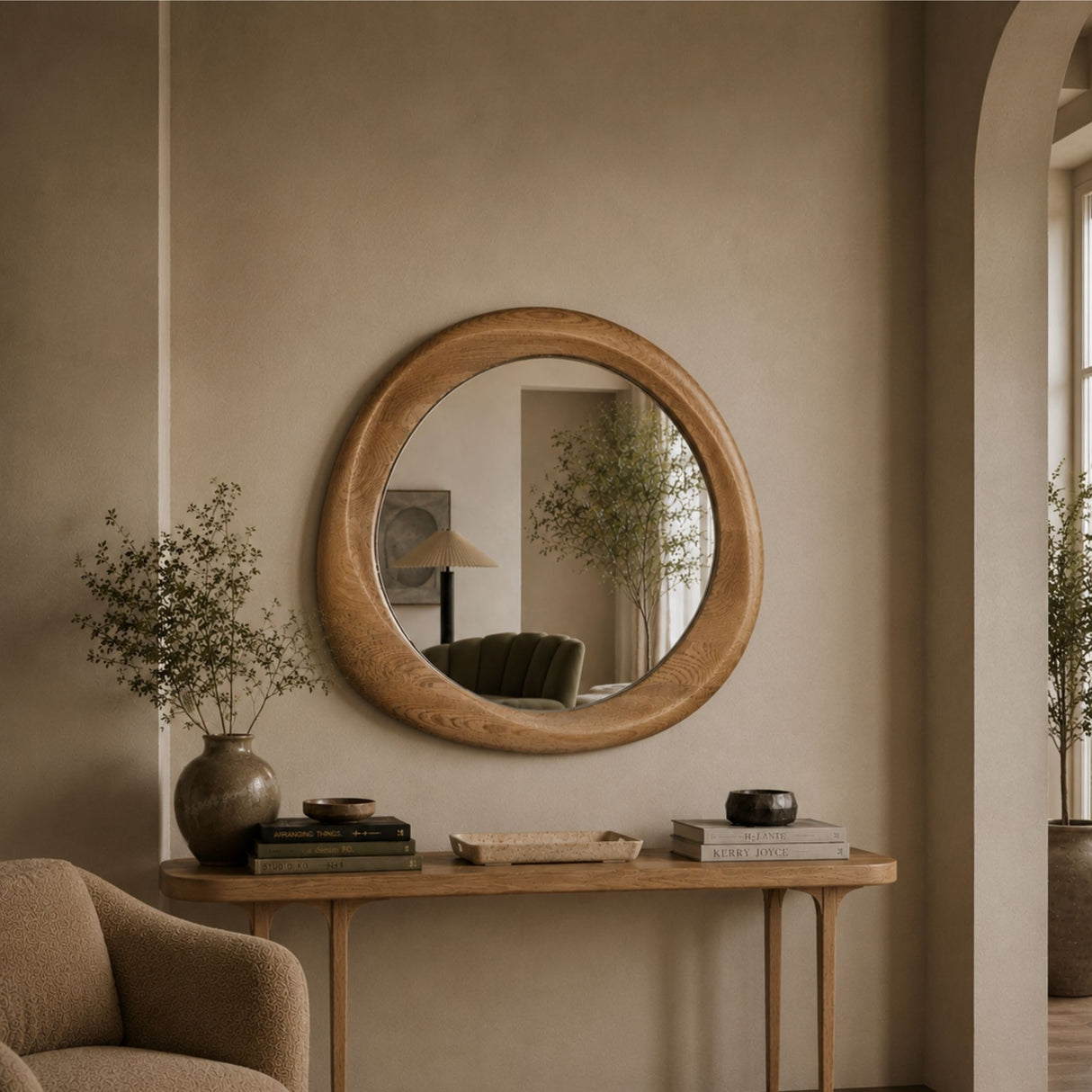 Round wooden wall mirror with a natural oak frame, hanging on a beige plaster wall above a wooden console table in a styled interior room.