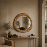 Round wooden wall mirror with a natural oak frame, hanging on a beige plaster wall above a wooden console table in a styled interior room.