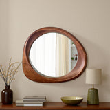 Round wooden mirror on a wall with decor items below