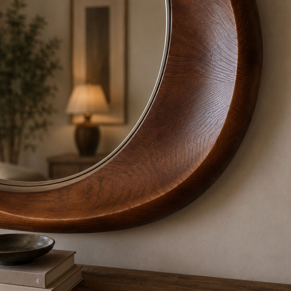 A close-up of a large round wall mirror with a thick, curved dark brown wooden frame, mounted on a beige wall above a wooden console table.